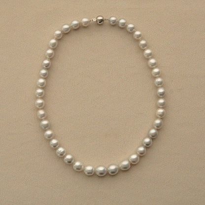 A classic strand of white Australian South Sea pearls arranged in an oval shape on a textured beige background, featuring a silver-toned clasp at the top.