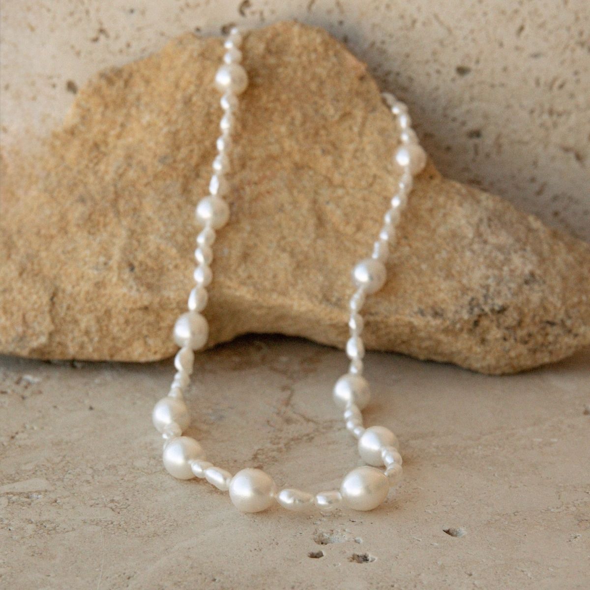 An Australian South Sea & Keshi pearl necklace draped over a natural tan rock on a textured stone surface.