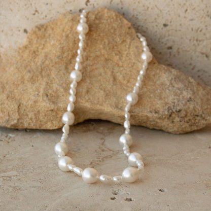 An Australian South Sea & Keshi pearl necklace draped over a natural tan rock on a textured stone surface.