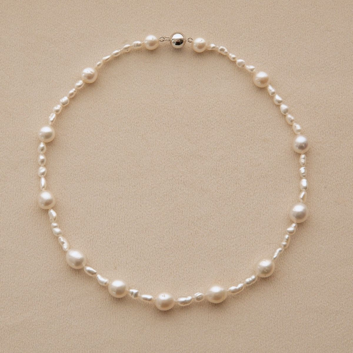 A delicate necklace made of white Australian South Sea & Keshi pearls, arranged in a circle on a textured beige background.