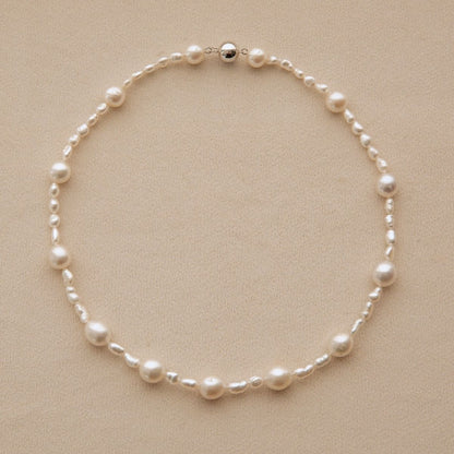 A delicate necklace made of white Australian South Sea & Keshi pearls, arranged in a circle on a textured beige background.