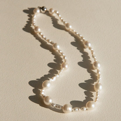An Australian South Sea & Keshi pearl necklace with mixed pearl sizes, styled on a textured beige surface with dramatic, sharp sunlight casting shadows.