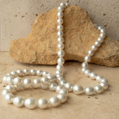 A three piece strand set of Australian South Sea pearl beads draped over a natural tan rock, set against a textured beige stone background.