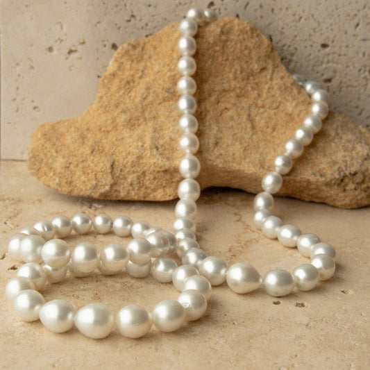 A three piece strand set of Australian South Sea pearl beads draped over a natural tan rock, set against a textured beige stone background.