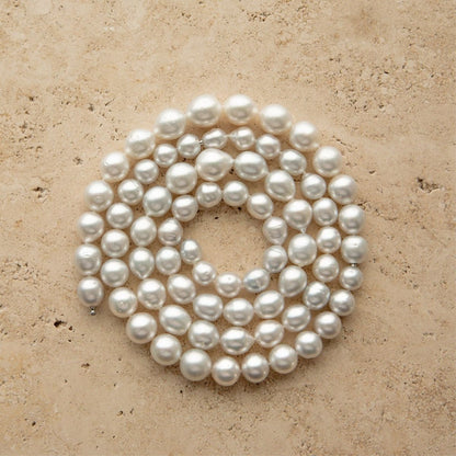 A coiled strand of Australian South Sea pearl beads in drop and semi drop shapes, arranged in a circle on a textured beige stone surface.