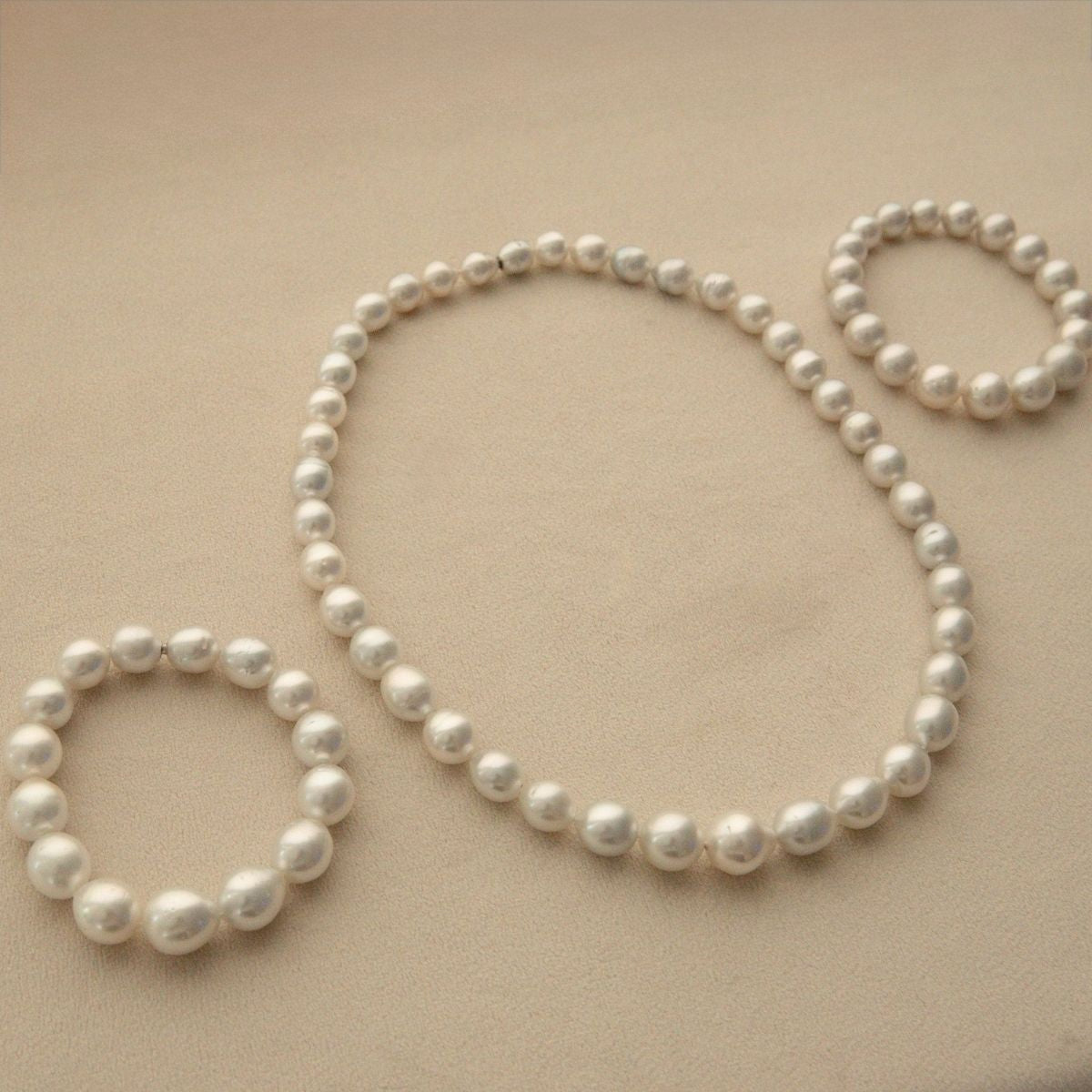 Three strands of Australian South Sea pearls arranged in a necklace and two bracelets, on a beige background.