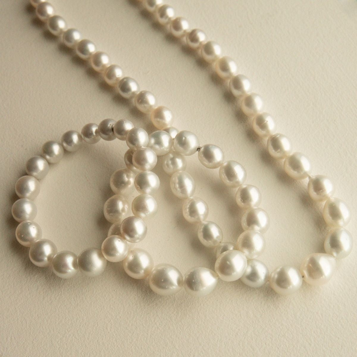 A set of  Australian South Sea pearl strands draped in overlapping loops on a light beige textured background.