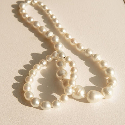 A strand of irregular baroque-style white South Sea pearls arranged in loops on a warm beige surface, casting soft shadows.