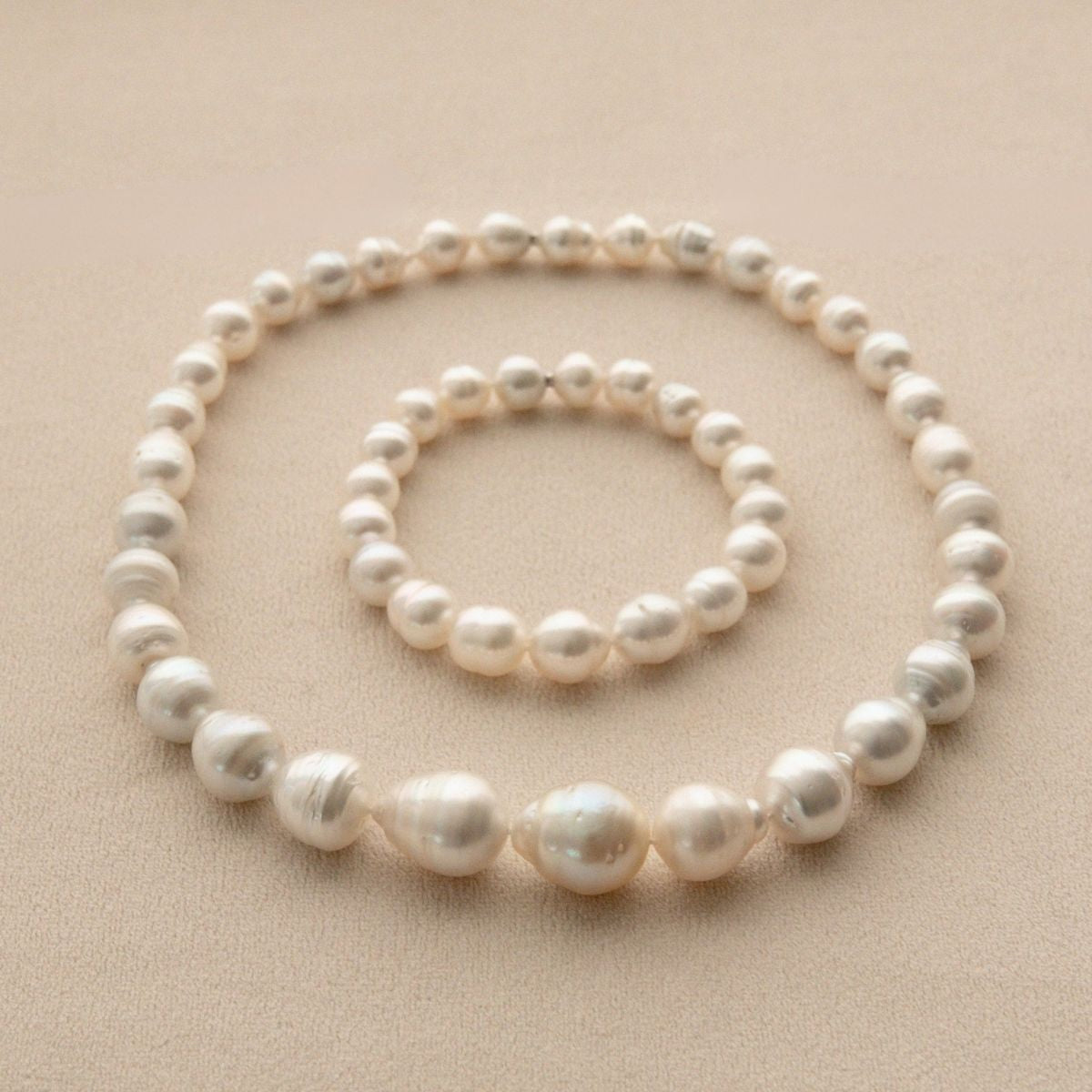A two piece set of Australian pearl jewellery, including a strand necklace and a matching bracelet, arranged in concentric circles on a textured beige background.