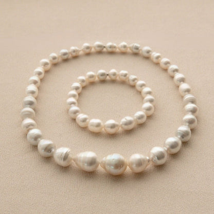 A two piece set of Australian pearl jewellery, including a strand necklace and a matching bracelet, arranged in concentric circles on a textured beige background.