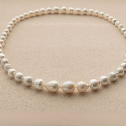 A strand of irregular white Australian South Sea pearls arranged in a circle on a textured beige background.