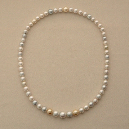 An Australian South Sea pearl necklace with mostly white and silver-gray pearls accented by a few gold and cream pearls, displayed on a neutral beige background.