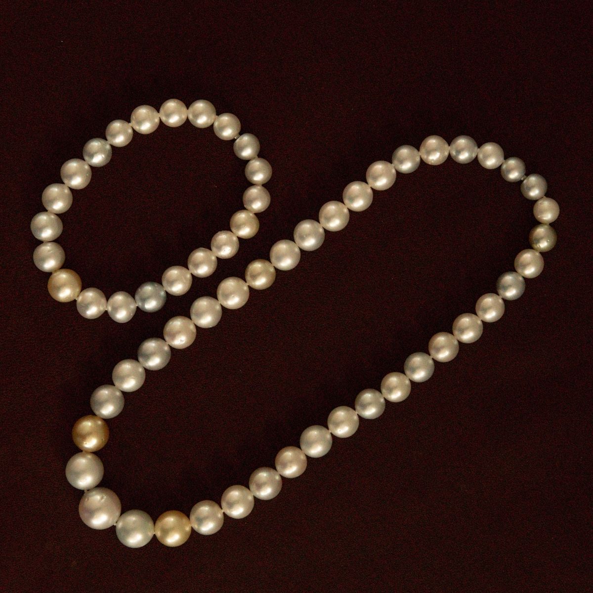A strand of multicolour Australian South Sea pearls arranged in its set of bracelet and necklace on a dark brown background.