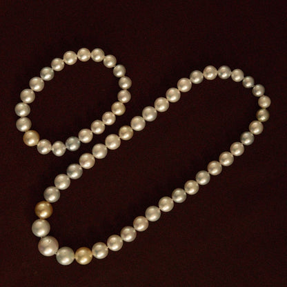 A strand of multicolour Australian South Sea pearls arranged in its set of bracelet and necklace on a dark brown background.
