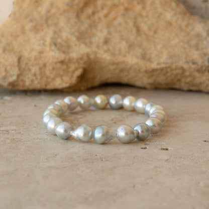 An Australian Akoya bracelet made of irregular, lustrous baroque Akoya pearls in multicolour tones, resting on a textured stone surface with a larger rock blurred in the background.