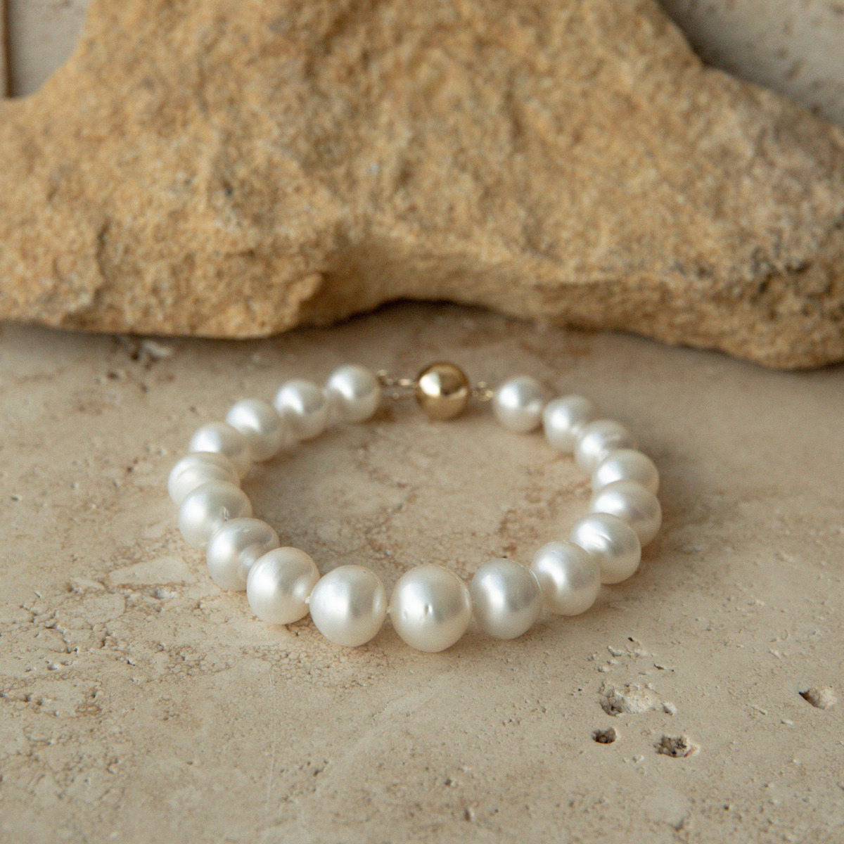 Pearl strand bracelet with a gold clasp on a stone surface