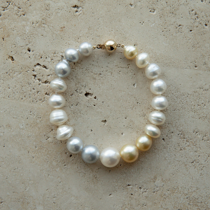 Pearl strand bracelet with gold clasp on a textured beige surface