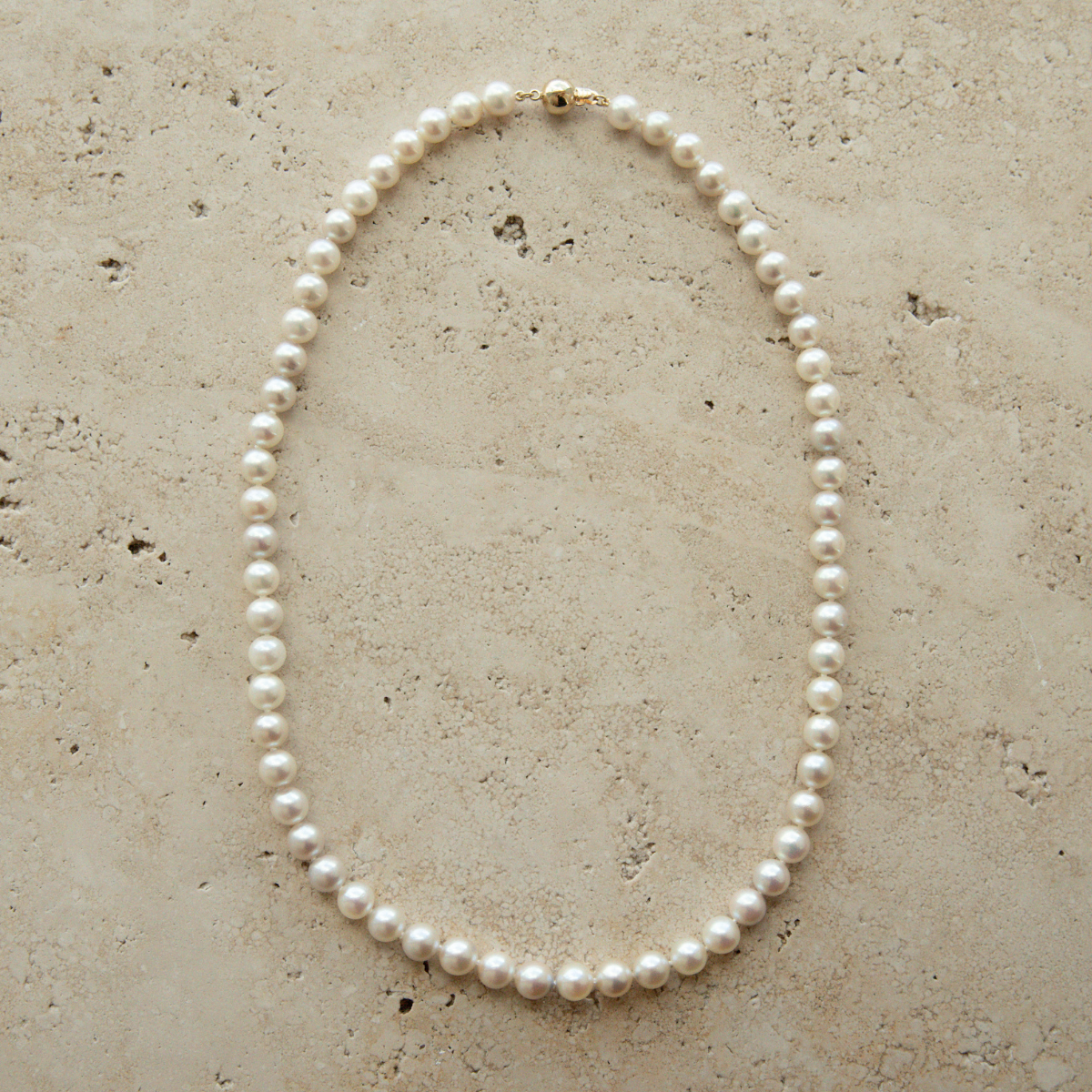 Pearl strand necklace on a textured beige surface