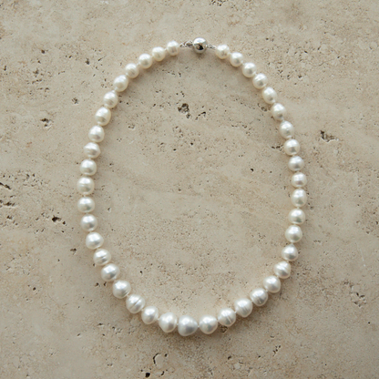 Pearl strand necklace on a textured beige surface