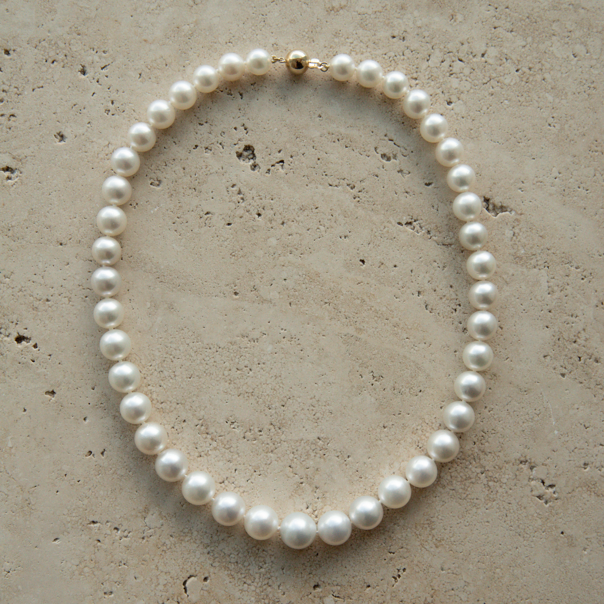 Pearl strand necklace on a textured beige surface