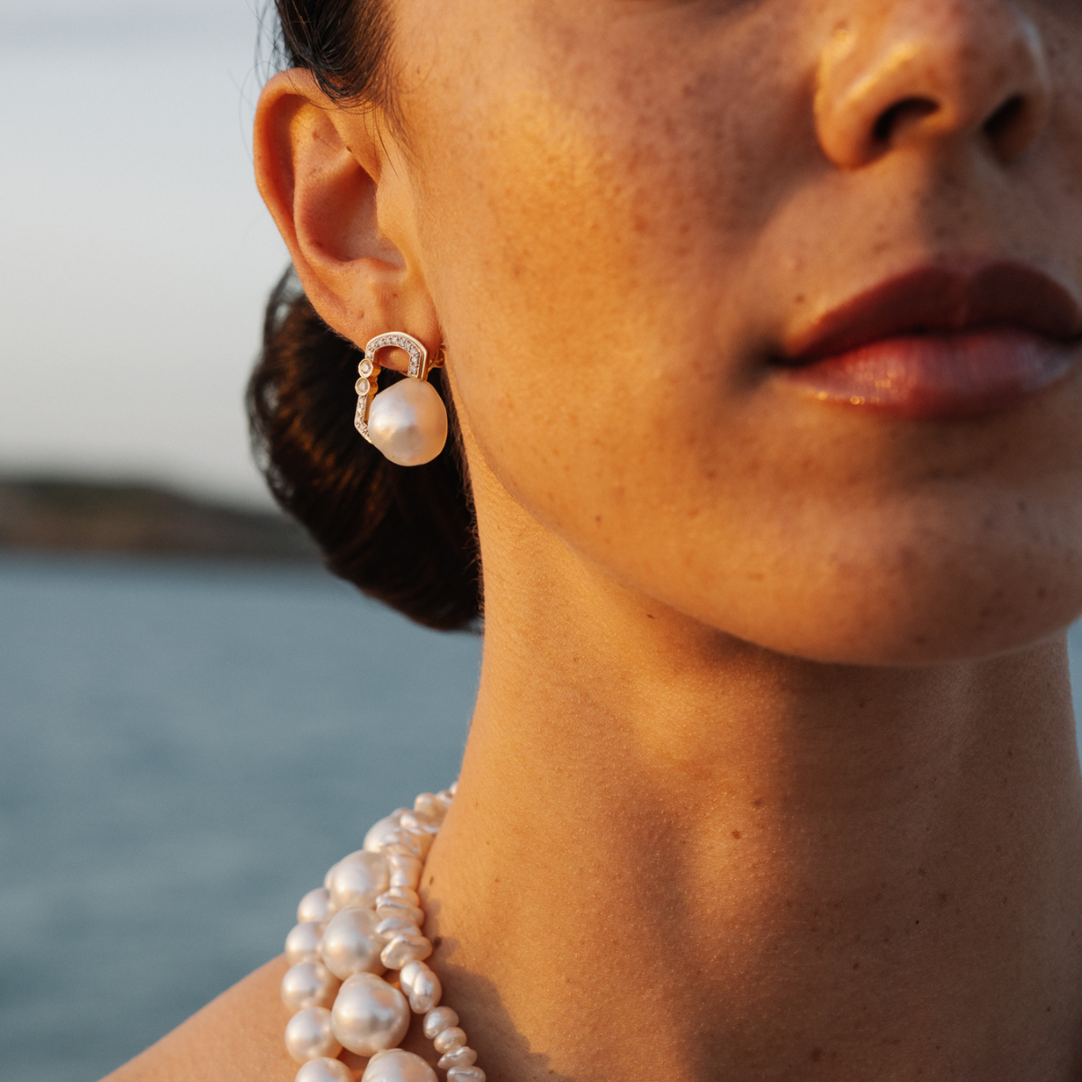 Close-up of a person wearing pearl earrings and a necklace with a blurred natural background