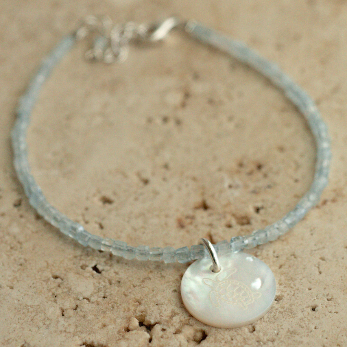 A unique Mother of Pearl charm bracelet featuring aquamarine gemstone beads, set in sterling silver.