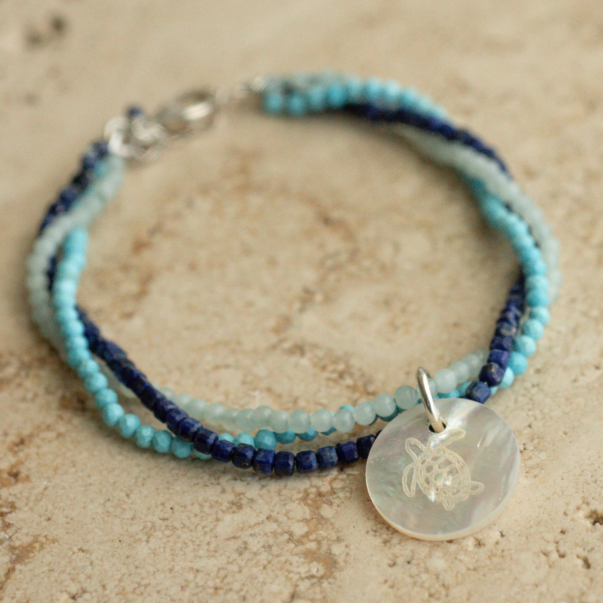 A unique Mother of Pearl charm bracelet featuring lapis lazuli, aquamarine, and turquoise gemstone beads, set in sterling silver.