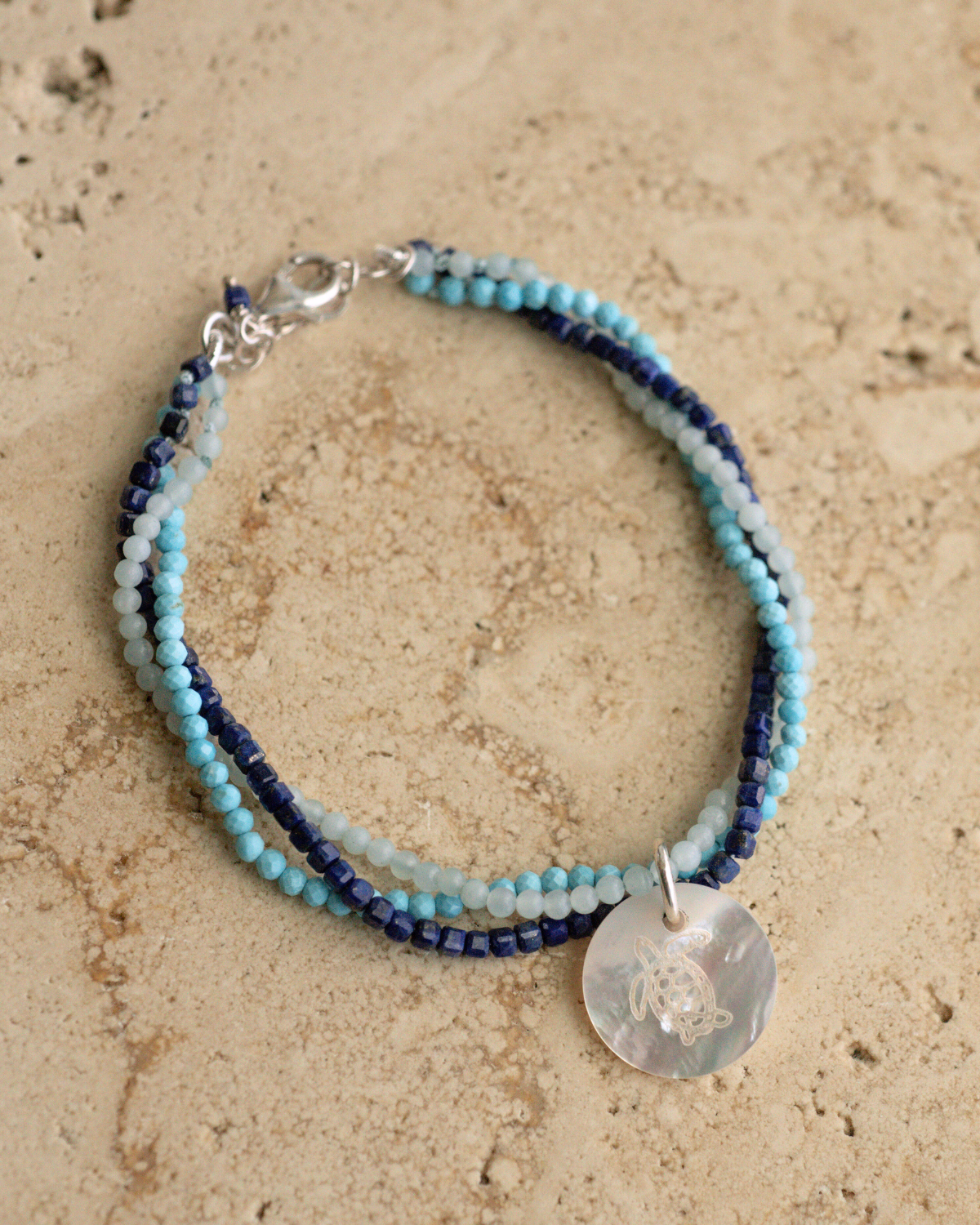 A unique Mother of Pearl charm bracelet featuring lapis lazuli, aquamarine, and turquoise gemstone beads, set in sterling silver.