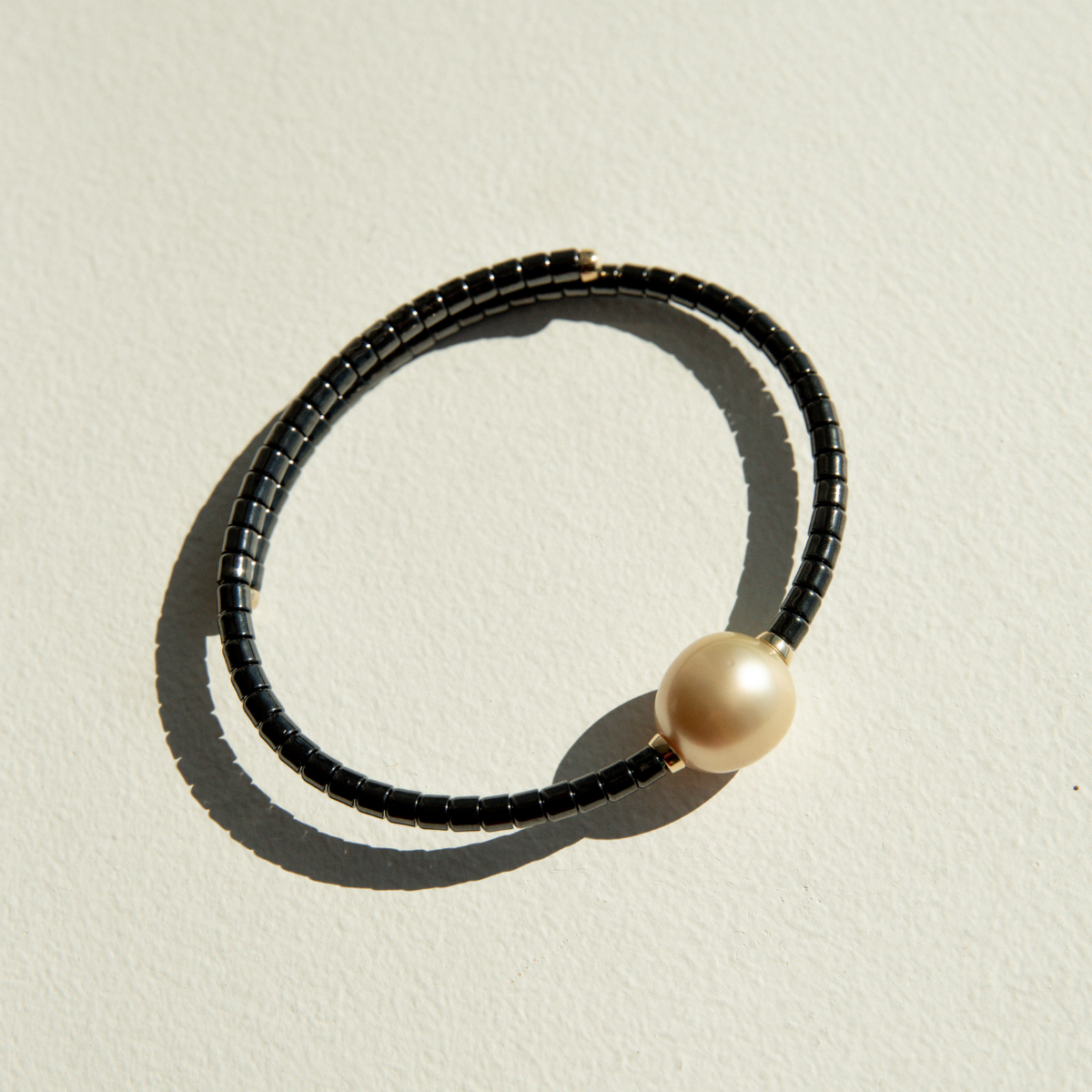 Bracelet with black ceramic links and a gold pearl on a sandy surface.