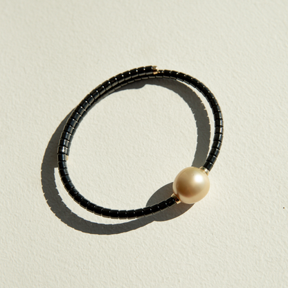 Bracelet with black ceramic links and a gold pearl on a sandy surface.