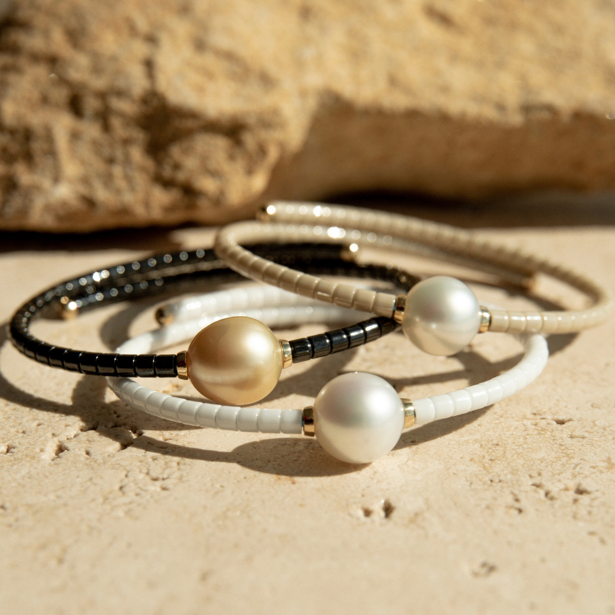 Three Bracelets with black, white and sand ceramic links and pearls on a sandy surface.