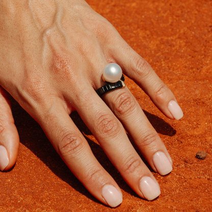 Hand wearing a pearl ring on an orange background