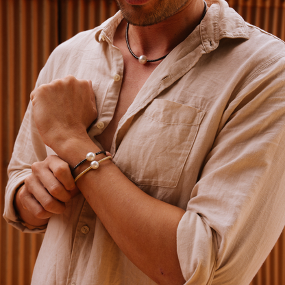 Man wearing a beige shirt with pearl accessories against a wooden background