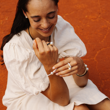 Woman in a white dress sitting against an orange wall, wearing jewelry.
