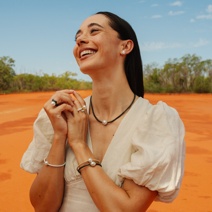Woman in a white blouse standing on red dirt with trees and blue sky in the background