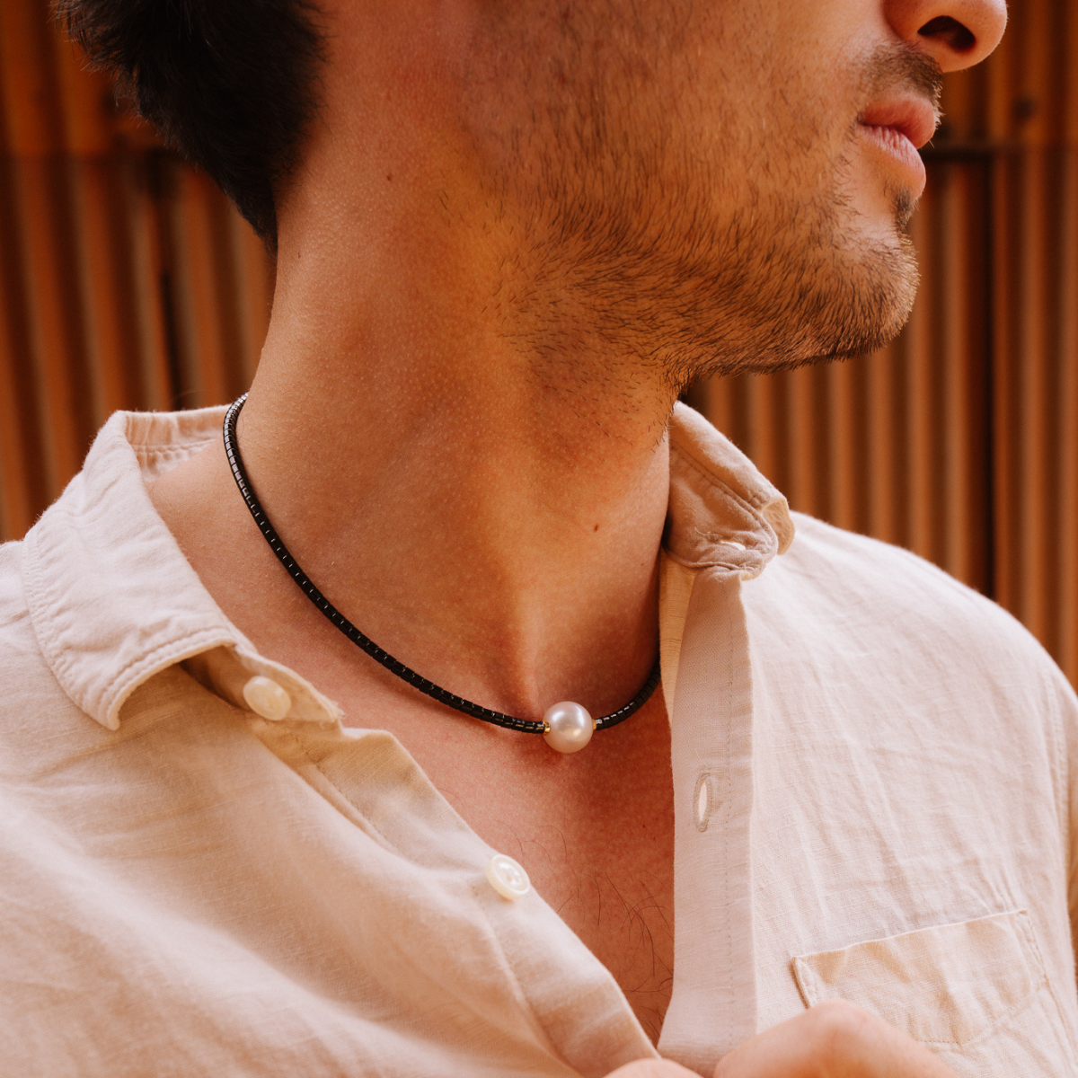Man wearing a white shirt with a black necklace featuring a pearl.