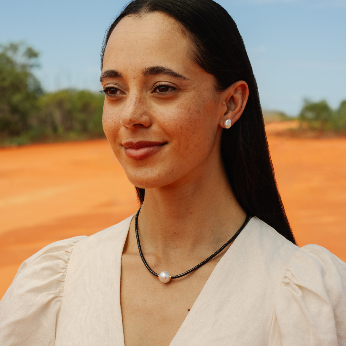 Woman with a pearl necklace standing in a desert-like landscape