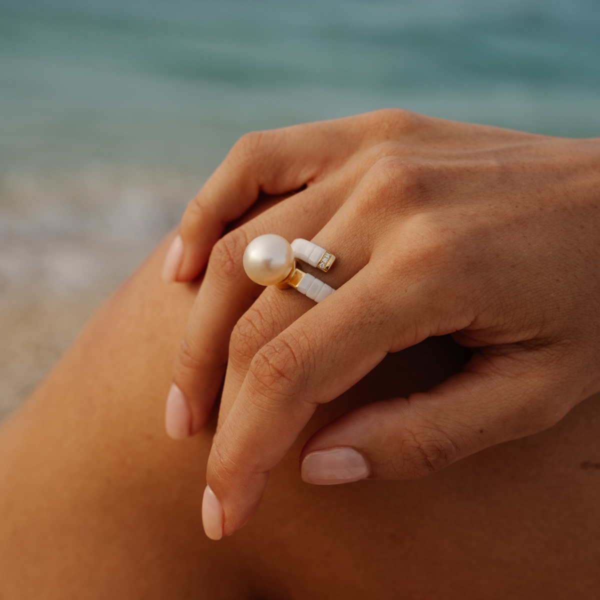 Hand with pearl and gold ring on a blurred beach background