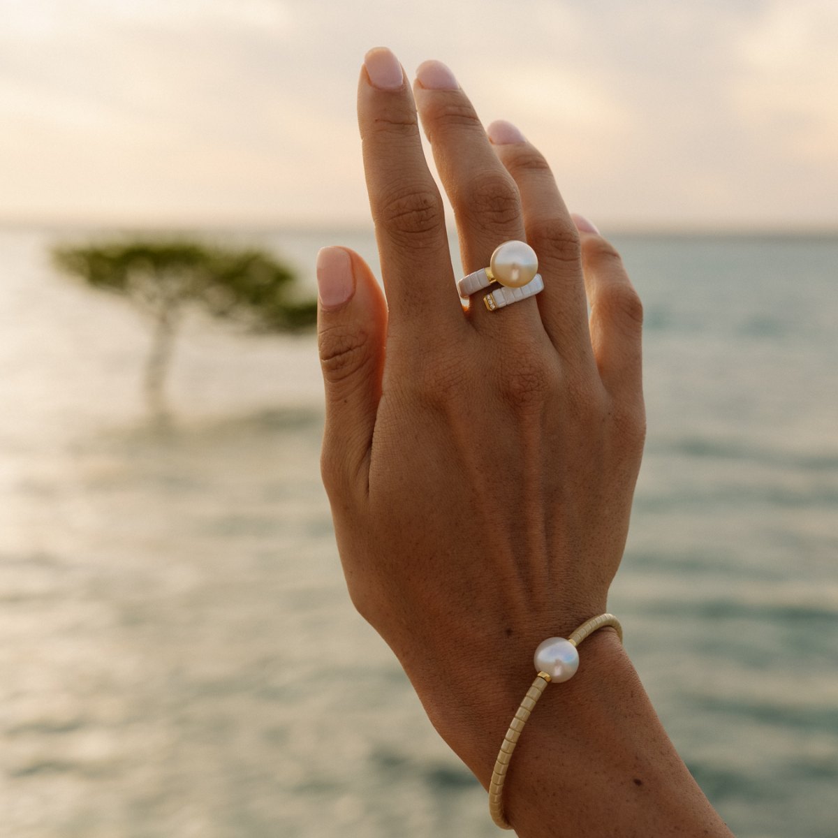 Hand wearing a pearl ring and bracelet with a blurred beach background