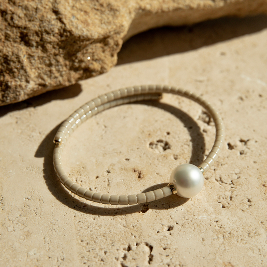 Beige ceramic bracelet with a pearl on a sandy surface.