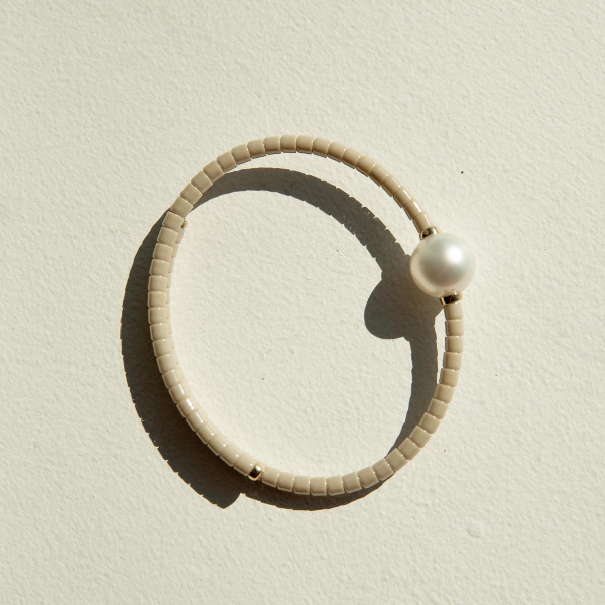 Beige ceramic bracelet with a pearl on a sandy surface.