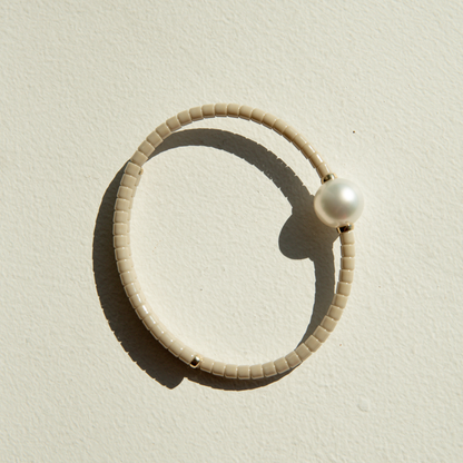 Beige ceramic bracelet with a pearl on a sandy surface.
