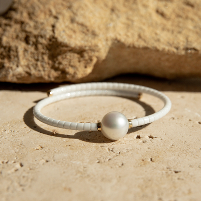 White ceramic bracelet with a pearl on a sandy surface.