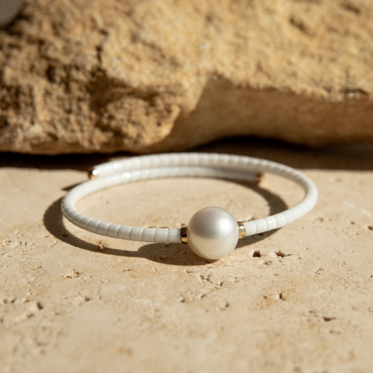 White ceramic bracelet with a pearl on a sandy surface.