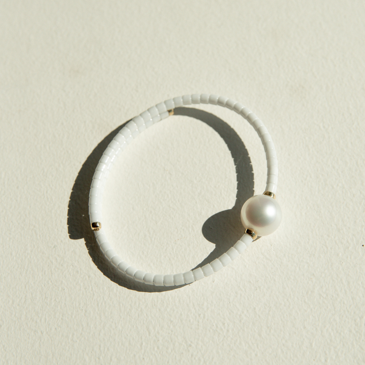 White ceramic bracelet with a pearl on a sandy surface.
