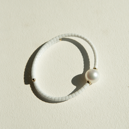 White ceramic bracelet with a pearl on a sandy surface.