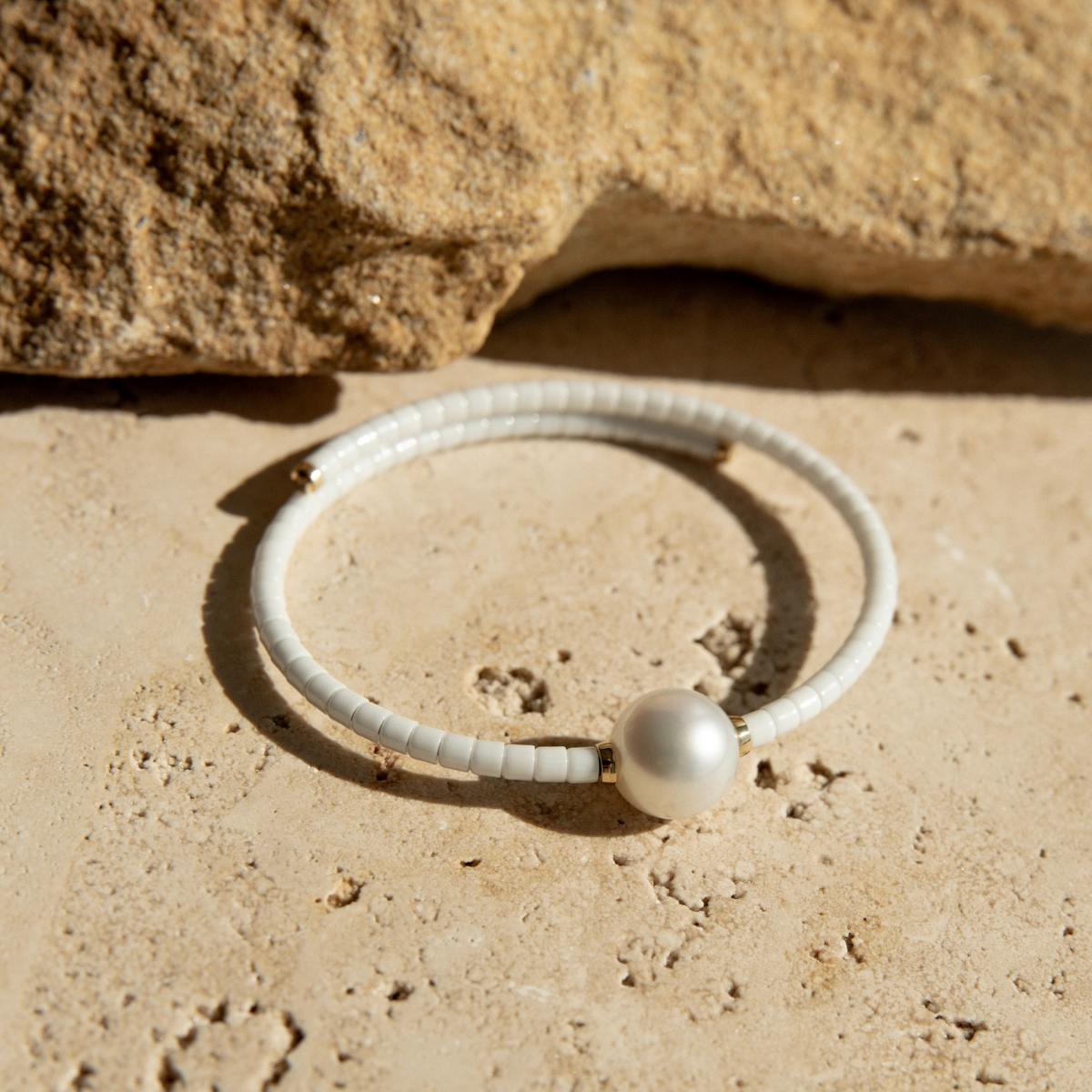 White ceramic bracelet with a pearl on a sandy surface.