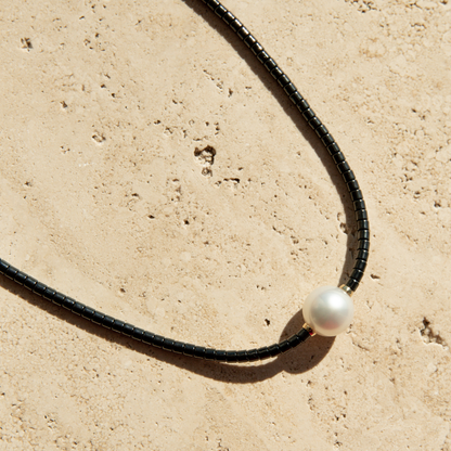 Black ceramic necklace with a single pearl on a beige stone surface
