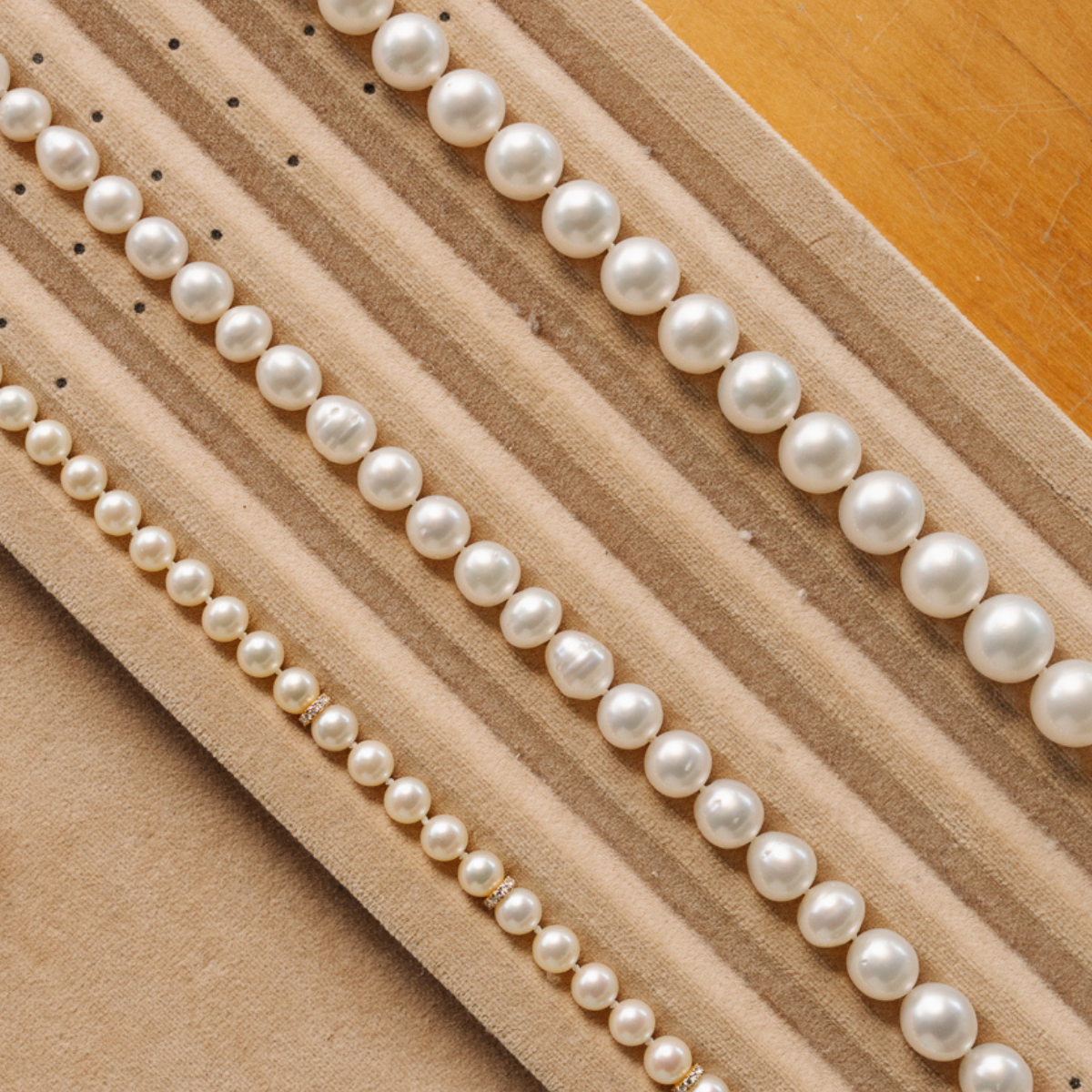 Three pearl strand necklaces, two of them Australian South Sea pearl strands and the other an Australian Akoya pearl strand sit on a textured beige surface, each pearl matched and graded based on their size, shape, colour, surface and lustre to create a stunning string of pearls.