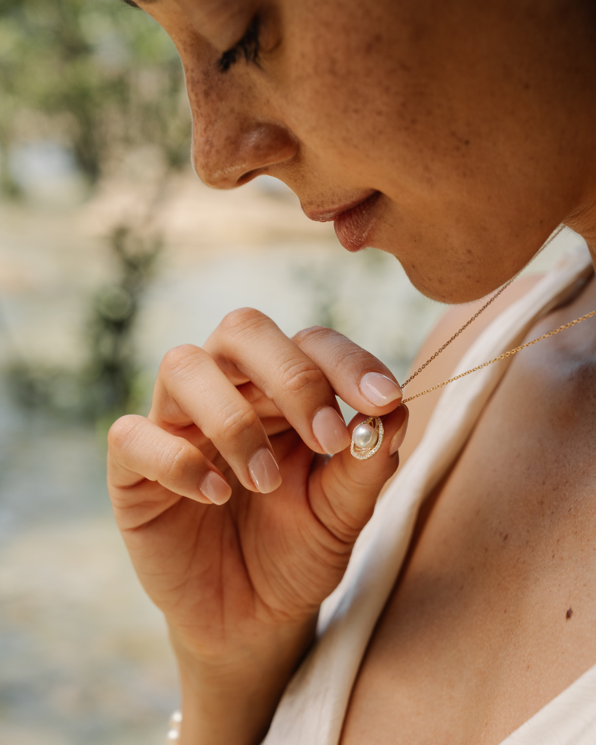 Person wearing a hypoallergenic Mangrove Lily diamond and pearl necklace with a blurred natural background